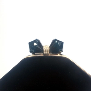 Macro detail of velvet evening clutch featuring a blue crystal bow clasp and gold frame