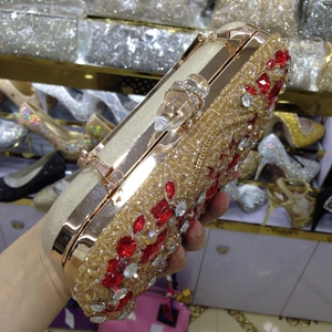 Detailed close-up of golden evening clutch bag featuring red gemstones and crystal beads