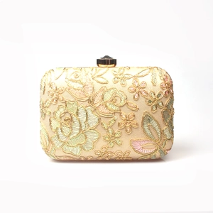Macro shot of 3D floral embroidery and gemstone clasp on gold evening clutch bag