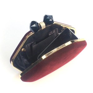 Macro detail of wine red velvet evening clutch featuring bow-shaped rhinestone clasp