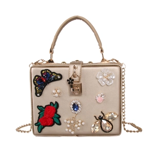 Detail view of golden evening clutch with butterfly embroidery, pearls and blue gemstone