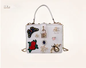 Detailed view of butterfly embroidery and floral rhinestones on white evening box bag