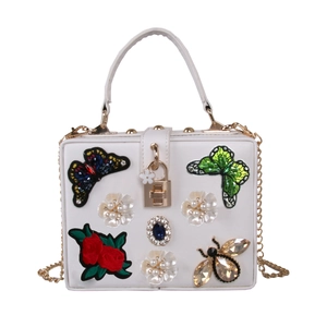 Close-up of white evening bag with butterfly embroidery, pearl flowers, and a rhinestone bee