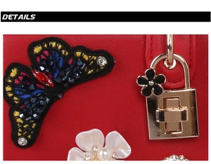 Detail of red leather bag with butterfly embroidery, flower accents, and gold twist lock