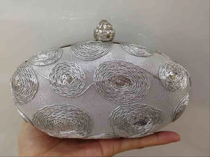 Detail of silver oval lace clutch bag with sequin swirls and a crystal clasp
