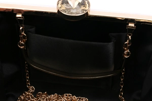 Detail of evening clutch featuring black satin lining, gold metal frame, and crystal clasp