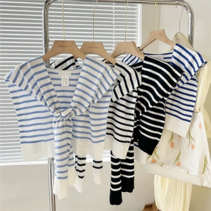 Trois châles en tricot rayé bleu et noir suspendus sur des cintres dans un studio