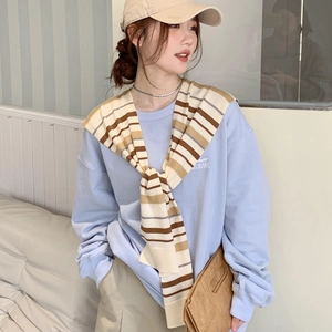 Close-up of a striped knitted shawl draped over a casual sweatshirt for a layered look