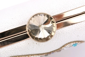 Macro detail of white glitter clutch bag with gold trim and large crystal jewel lock