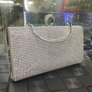 Macro detail of silver crystal evening clutch featuring a round diamond buckle and chain