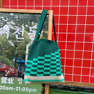 Detail of dark green knit tote bag with lime green checkered pattern on wooden stand