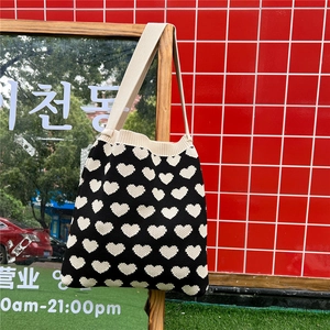 Detail of a black knitted heart pattern tote bag hanging on a display stand in a street setting