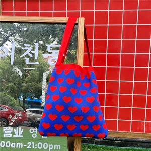 Detail of blue knit tote bag with red heart jacquard pattern hanging on wooden stand