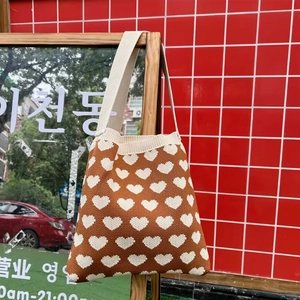 Detail of knitted tote bag with brown heart pattern and creamy white strap on a wooden rack