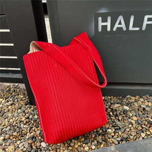 Detailed close-up of bright red pleated knit tote bag with vertical stripes in outdoor setting