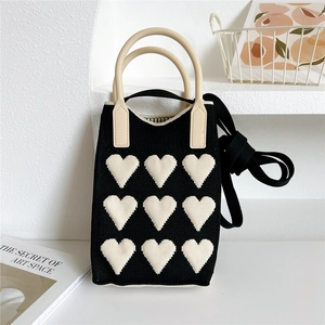 Close-up of black knit tote bag with white heart patterns and beige round handles