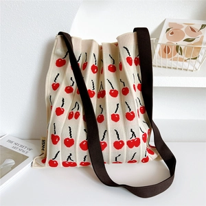 Detail view of cream pleated knitted tote bag with red cherry pattern and brown straps