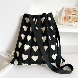 Close-up of pleated knit texture and cream heart pattern on a black shoulder tote bag