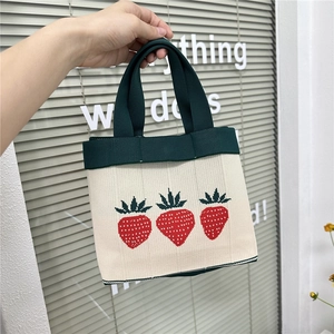 Mini knitted tote bag with red strawberry embroidery and green handles held by hand