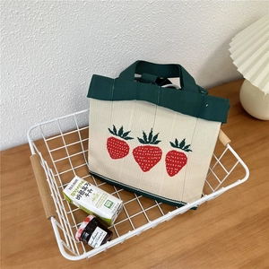 Close-up of a knitted mini tote bag with red strawberry patterns in a picnic setting