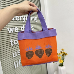 Close-up of orange knitted tote bag featuring purple handles and strawberry pattern details
