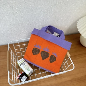 Detail of vibrant orange knit tote bag with purple handles and strawberry pattern