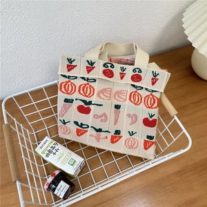 Detailed close-up of a knit tote bag with strawberry patterns in a rustic basket