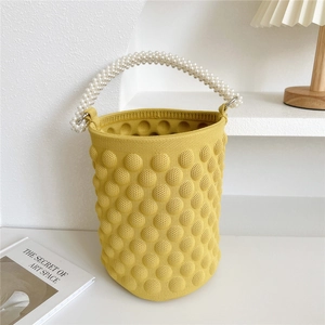 Close-up of ginger yellow popcorn knit bucket bag with elegant faux pearl beaded handle