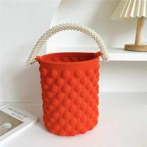 Detail of orange popcorn knit bucket bag with elegant pearl handle on a white surface