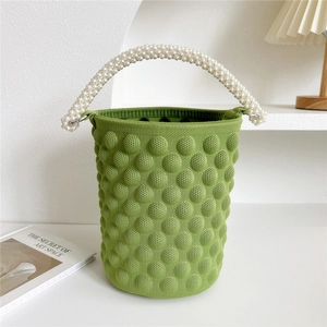 Close-up of green knitted bucket bag featuring textured dots and pearl beaded handle