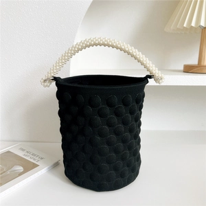 Detail of black knit bucket bag featuring a white pearl handle in a minimalist setting
