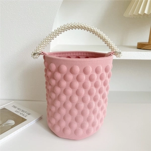 Detailed texture of pink knitted bucket bag featuring 3D puff balls and pearl handles