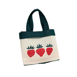 Off-white knitted tote bag with green handles and red strawberry jacquard pattern