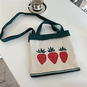 Detail of knitted shoulder bag with red strawberry patterns and green handles