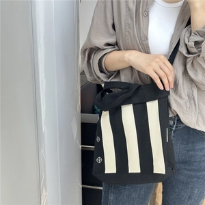 Black and white striped knit tote bag with shoulder strap and minimalist side badge