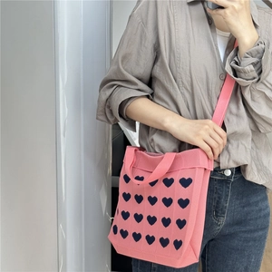 Pink knitted tote bag with blue heart pattern, featuring top handles and shoulder strap