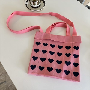 Detailed top view of pink knitted tote bag with heart patterns on a white table
