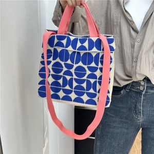 Detail of knitted tote bag with blue geometric dots and coral pink straps held by hand
