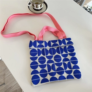 Detail of blue and white geometric knit tote bag with pink woven straps on white surface
