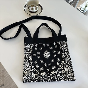 Black and white paisley knit tote bag with shoulder strap on a table with coffee cup