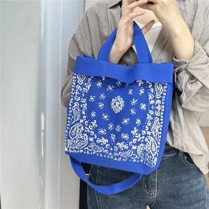 Blue knit tote bag with white paisley patterns and shoulder strap detail shown on model