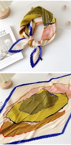 Detail view of a pleated geometric square scarf featuring color block designs and silk texture