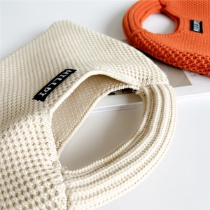 Detail of cream white and orange chunky knit tote bag with 3D mesh texture and brand label