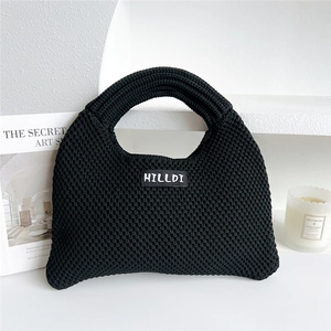Close-up of a black knitted tote bag with a minimalist brand label on white desk