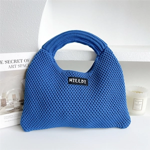 Close-up of blue chunky knit tote bag with brand logo label on minimalist white surface