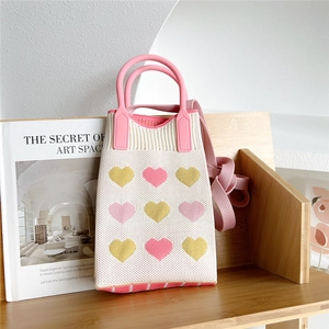 Detail of white knitted crossbody bag with colorful hearts and pink handles