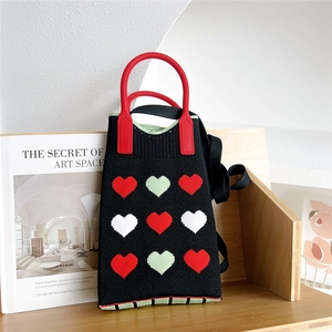 Close-up of a knit mini tote with heart patterns and a red circular handle on a shelf