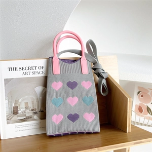 Detail of grey knitted bag with heart jacquard pattern and pink round handle on bookshelf