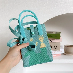 Close-up of mint green knitted handbag featuring a yellow giraffe pattern and gemstone buckle