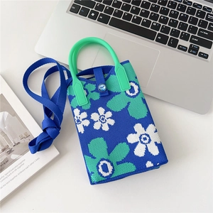 Detail of floral knit phone bag featuring green handle and blue woven shoulder strap